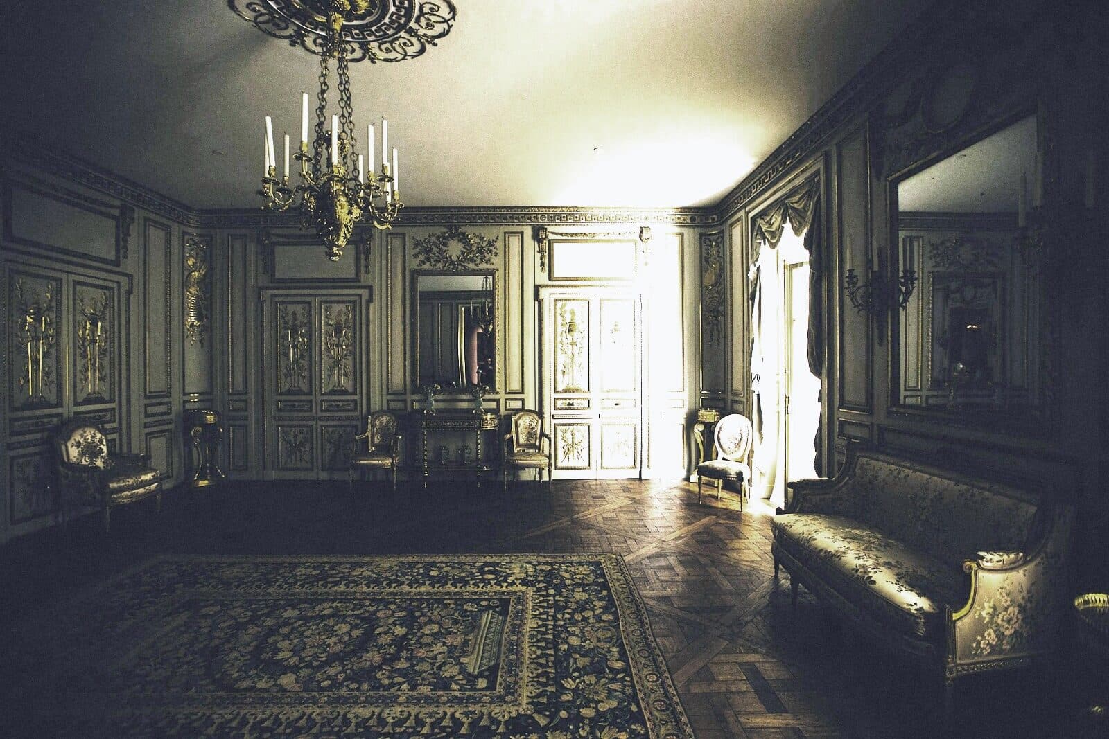A hotel corridor under a chandelier, light spilling from an open door