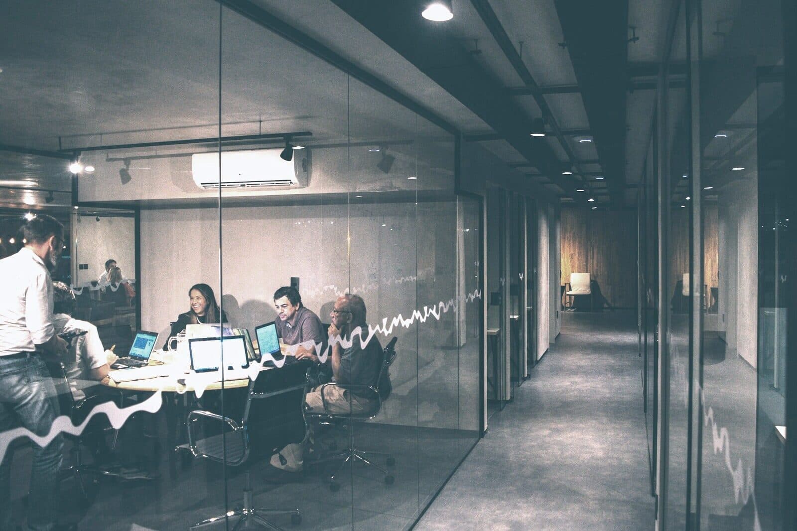 A client review meeting under low light in a glass-walled room