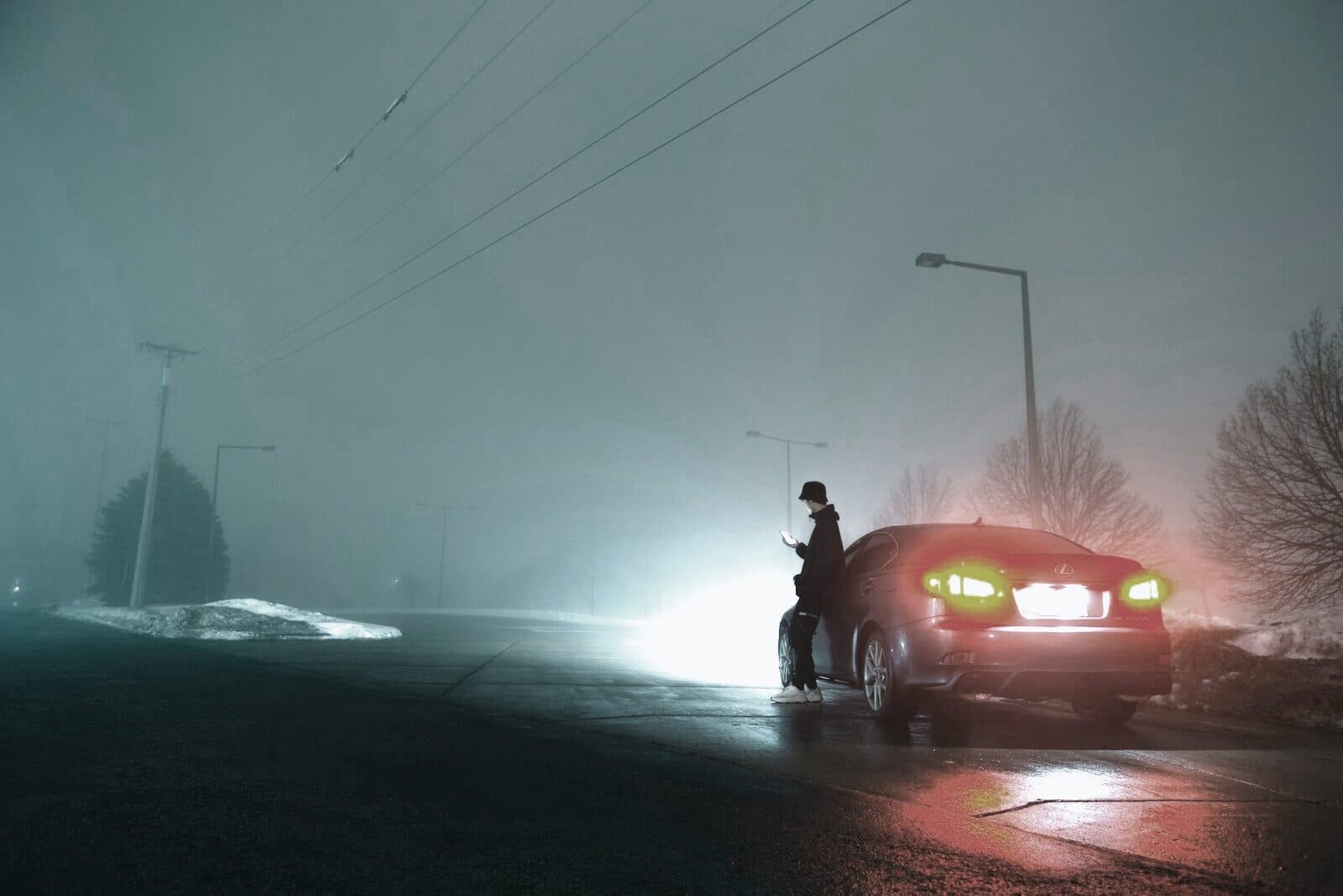 A lone figure beside a car on a fog-bound road at night